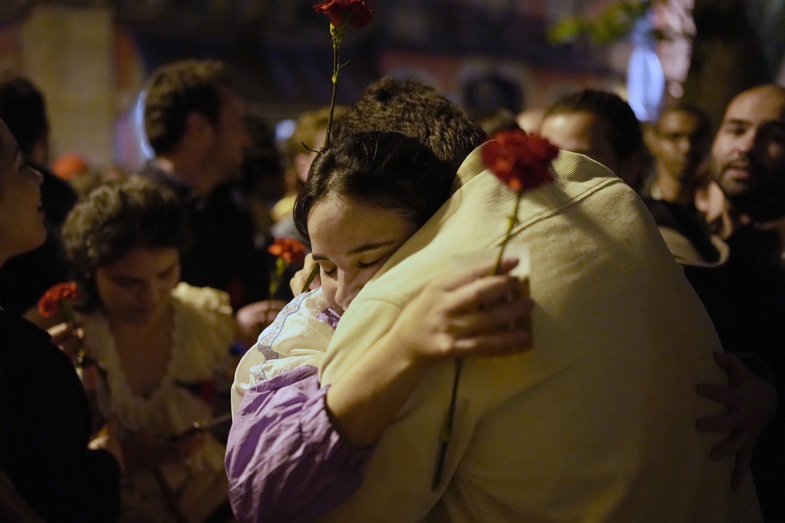 A couple hold red carnations while embracing each other after thousands sang the folk song Grandola, Vila Morena, in the first minutes of Thursday, April 25, 2024, at the Carmo square in Lisbon, as th ...