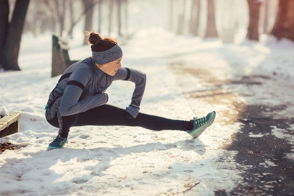 Female runner jogging in the forest on winter day. Crouching and streching after running