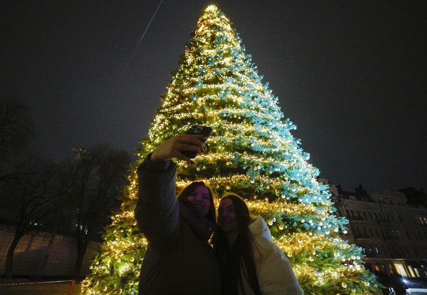 epa12572767 People take a selfie with the Christmas tree after the turning on the light illumination in front of Saint Sophia's Cathedral in Kyiv, Ukraine, 05 December 2025. For the third year, U ...