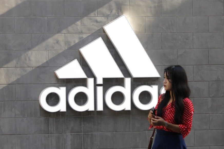 epa07591449 A Chinese woman walks past a logo of Adidas outside Adidas store in Beijing, China, 22 May 2019. A letter signed by 173 companies which including Nike, Adidas, says the US President&#039;s ...