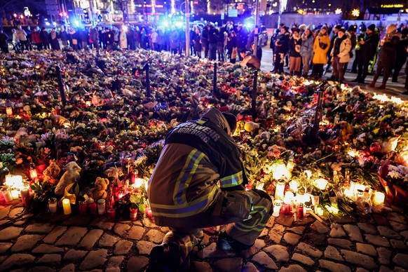 epaselect epa11791323 A firefighter in front of candles and flowers at the mourning site in front of St. John&#039;s Church following a vehicle-ramming attack on the Christmas market in Magdeburg, Ger ...
