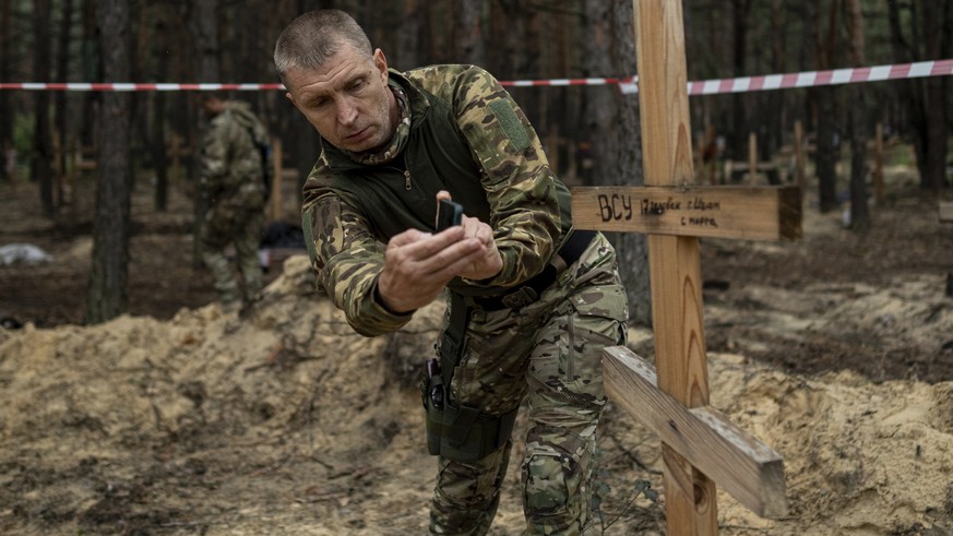 Oleg Kotenko, the Commissioner for the Issue of Missing Persons under Special Circumstances, uses his smartphone to film the grave of a Ukrainian soldier in the recently recaptured area of ​​Izium, Ukraine, Thursday...
