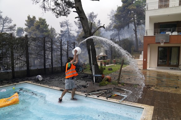 A man throws water from a swimming pool as the fire approaches his house in Ippokratios Politia village, about 35 kilometres (21 miles) north of Athens, Greece, Friday, Aug. 6, 2021. Thousands of peop ...