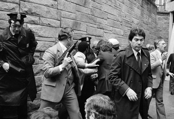 FILE - In this Monday, March 30, 1981 file photo, Secret Service agents and police officers swarm a gunman, obscured from view, after he attempted an assassination on President Ronald Reagan outside t ...