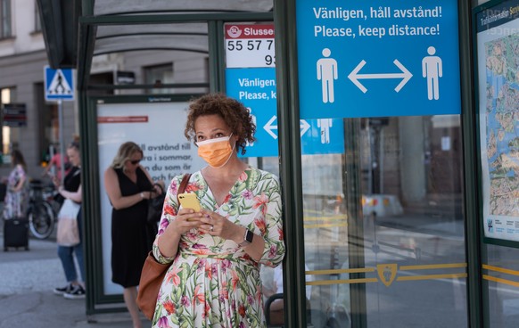 epa08510994 A woman wearing a face mask stands at a bus stop featuring a sign reminding passengers to maintain a minimum social distance between each other to reduce the risk of infection with the SAR ...