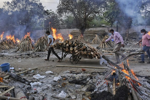 A worker carries wood on a hand cart as multiple funeral pyres of COVID-19 victims burn at a crematorium on the outskirts of New Delhi, India, Saturday, May 1, 2021. India on Saturday set yet another  ...