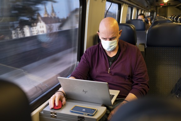 Passenger wearing protective mask works on a laptop as he rides a SBB CFF FFS train during the coronavirus disease (COVID-19) outbreak, in Neuchatel, Switzerland, Tuesday, March 23, 2021. Switzerland  ...
