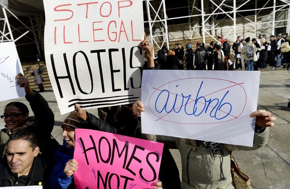 epa04571218 Detractors of Airbnb operations in New York hold signs during a rally while supporters of the company (R) wait in line to enter City Hall before a hearing on the subject of Airbnb in New Y ...