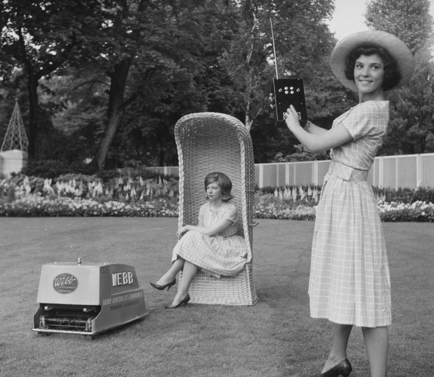 Two women, one sitting in a wicker garden chair while the other stands with the controller of the Webb radio-controlled electric lawnmower in the Jardin du Luxembourg in Paris, France, 24th May 1960.  ...