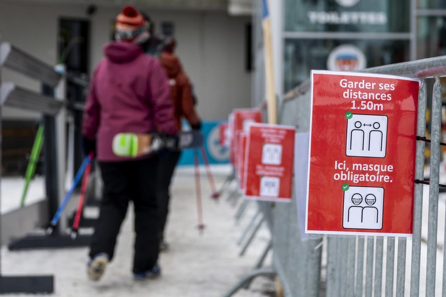 Des skieurs passent devant une affiche de la station de ski de Verbier informant de distanciations sociales pour les skieurs au depart des telecabines a Medran lors de la crise du Coronavirus (Covid-1 ...