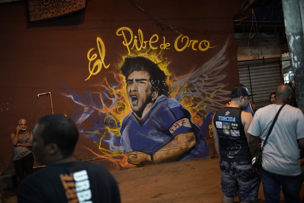 People stand next to a mural made by graffiti artist Angelo Campos in honor of late Argentina's soccer legend Diego Maradona at a favela in Rio de Janeiro, Brazil, Wednesday, Nov. 25, 2020. The D ...