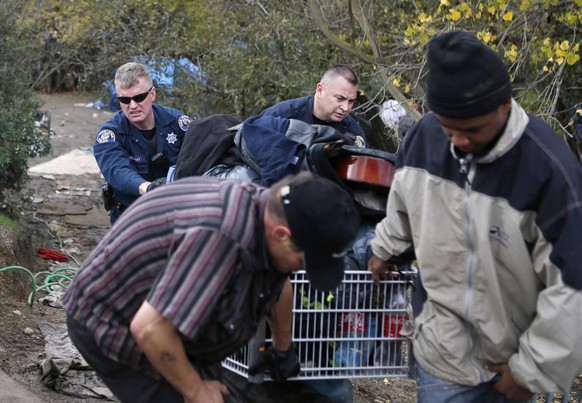 Polizisten unterstützen einen Obdachlosen dabei, sein in einem Einkaufswagen gesammelten Hab und Gut aus dem Camp zu räumen.
