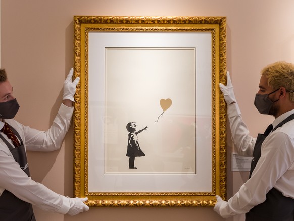 epa09473437 Art handlers display an artwork by Banksy called &#039;Girl with Balloon (Colour)&#039; at Christie&#039;s auction rooms in London, Britain, 17 September 2021. The plate will be up for auc ...