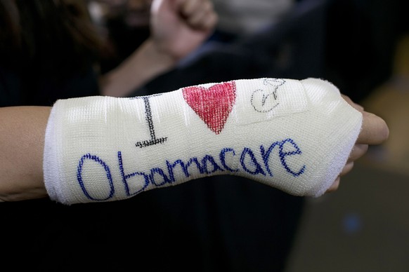 epa07232852 (FILE) - A supporter wears a cast on her broken wrist with &#039;I (heart) Obamacare&#039; written on it as US President Barack Obama gives his speech on the Affordable Care Act inside his ...