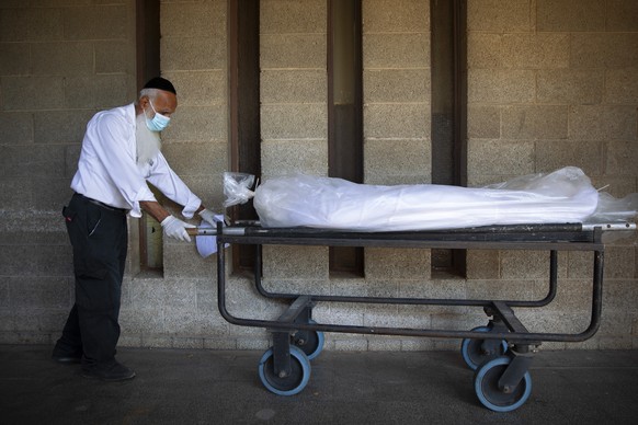 A worker from &quot;Hevra Kadisha,&quot; Israel's official Jewish burial society, caries a body before a funeral procession at a special morgue for COVID-19 victims, during a nationwide lockdown to cu ...
