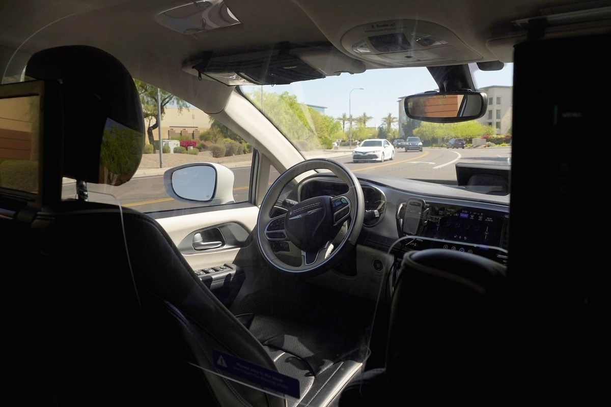 FILE - A Waymo minivan moves along a city street as an empty driver's seat and a moving steering wheel drive passengers during an autonomous vehicle ride, on April 7, 2021, in Chandler, Ariz. The ...