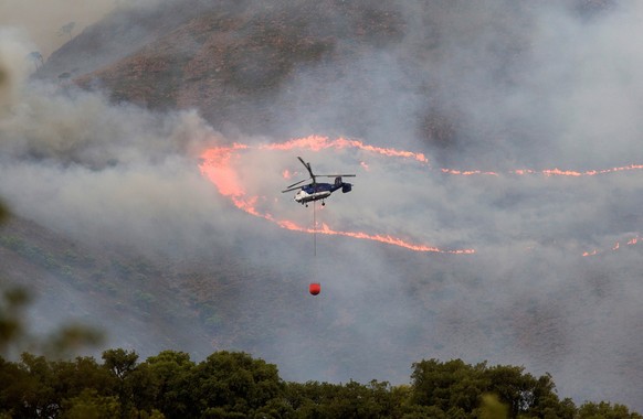 epa09466056 An helicopter pours water onto the forest fire in Sierra Bermeja, Malaga, Spain, 13 September 2021. The fire has burned over 7,800 hectares of Estepona municipality as Emergency Services w ...