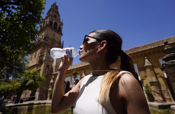 epa10006132 A woman drinks an iced water to cool herself as she visits the Courtyard of the Orange Trees in Cordoba, southern Spain, 10 June 2022. A heat wave is affecting the country with temperature ...