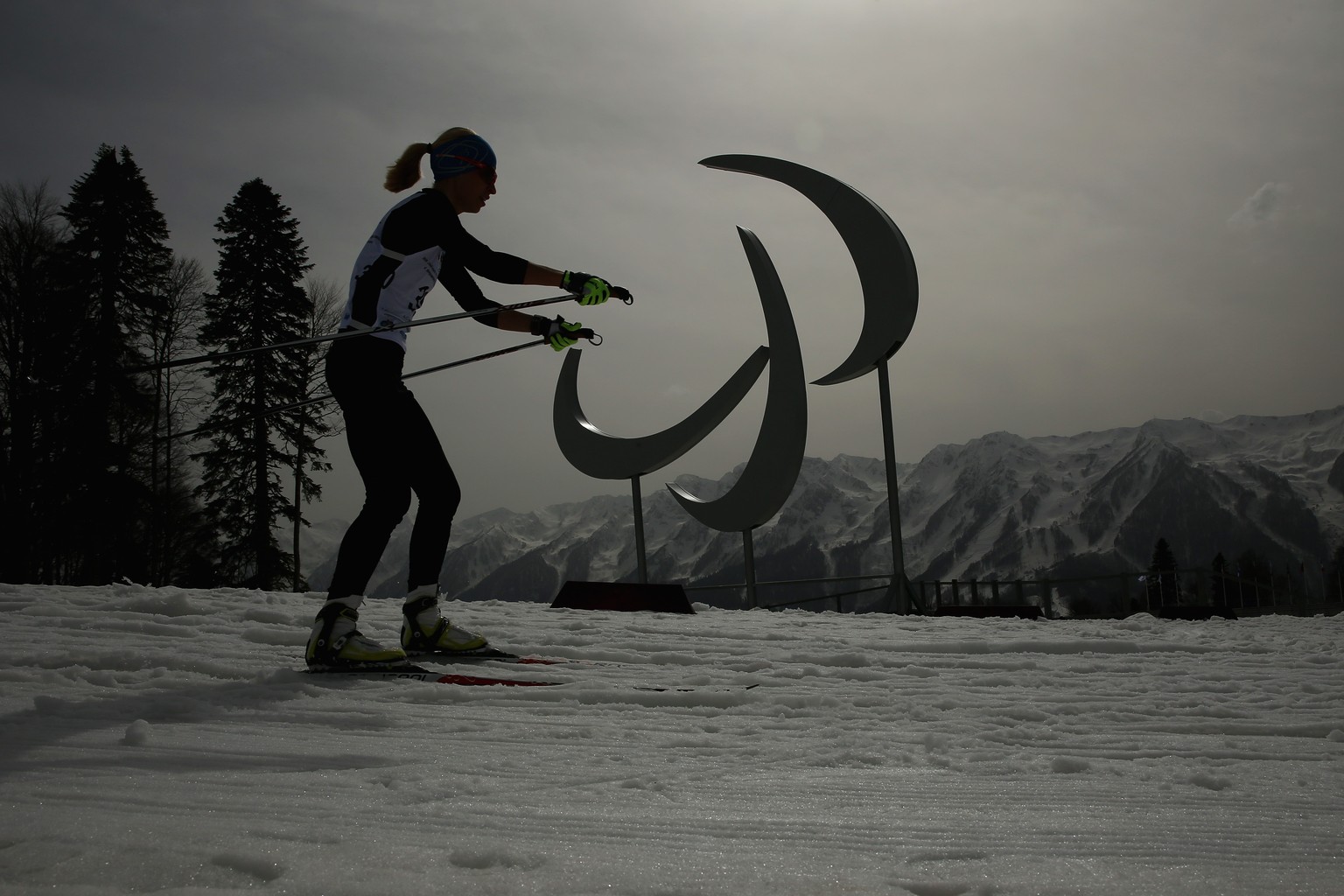 Eine Langläuferin beim Training. Im Hintergrund das Symbol der Paralympics.