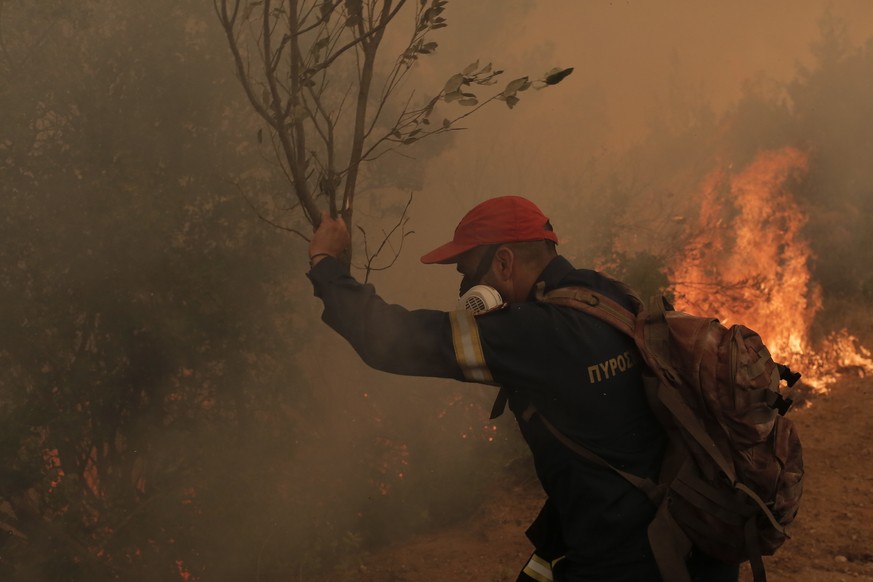 epa09407197 A firefighter uses tree branches, due to water shortage, while battling flames during a wildfire at the village of Istiaia in the island of Evia, Greece, 09 August 2021. Fires that broke o ...