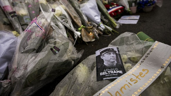 A photo of Lieutenant Colonel Arnaud Beltrame placed on flowers at the main gate of the Police headquarters in Carcassonne, France, Saturday, March 24, 2018, following an attack on a supermarket in Tr ...