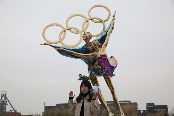 epa09591023 A woman poses for photo beside a statue of figure skaters with Olympic Rings near the headquarters of the 2022 Beijing Winter Olympics organising committee, at Shougang Park in Beijing, Ch ...