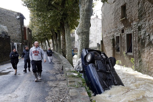 epa07094477 People walk pass a submerged car due to heavy rain falls and violent storm that hit Aude department overnight in Villegailhenc, France, 15 October 2018. According to a recent media report  ...