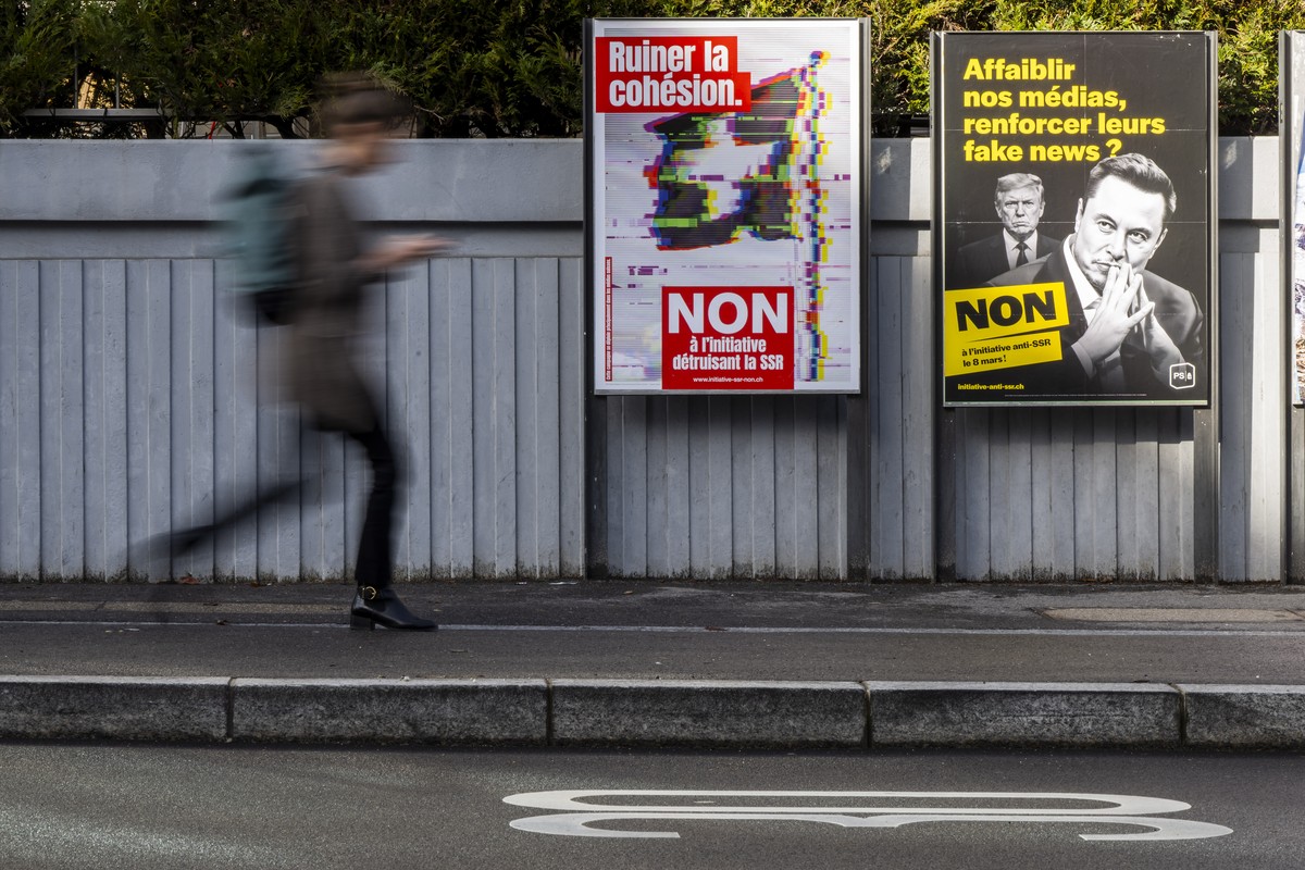 Une personne passe devant des affiches de la campagne du "Non a la reduction de moitie de la SSR", portant le slogan "Ruiner la cohesion", et "Contre l'initiative populai ...