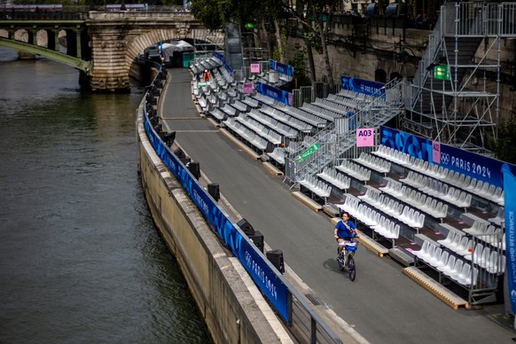 epa11495638 A woman rides bike past tribunes on the bank of Seine river prior to opening ceremony of the Paris 2024 Olympic Games, in Paris, France, 25 July 2024. The opening ceremony of the Paris 202 ...