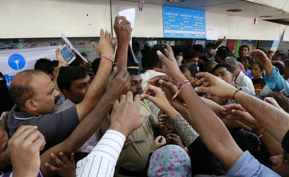 Indians stretch out their hands to collect withdrawal slips from a police officer to deposit and exchange discontinued currency notes outside the State bank of India in Mumbai, India, Thursday, Nov. 1 ...