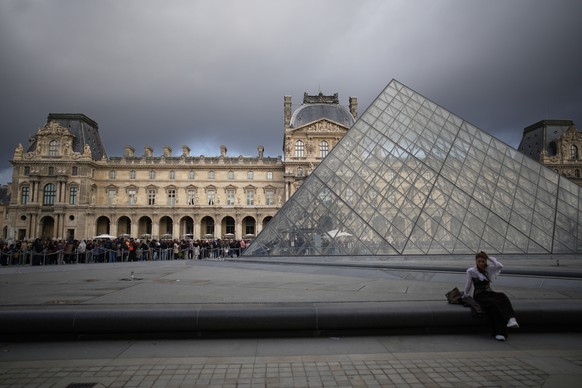 A woman sits while people queue to enter Le Louvre museum Monday, Oct. 27, 2025 in Paris. (AP Photo/Christophe Ena)
France Louvre