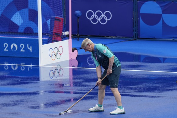 A volunteer removes excess water from the pitch after a malfunction in spraying system during a beak between the matches at the Yves-du-Manoir Stadium, the venue for field hockey competition, during t ...