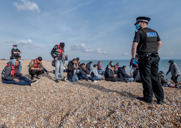 epa10199029 Police officers stand next to migrants who were rescued in the English Channel, at Dungeness, Britain, 22 September 2022. According to the British Ministry of Defence, more than 30,000 peo ...