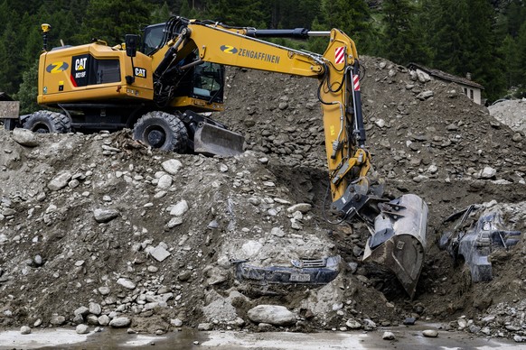 Une pelleteuse enleve des gravats entre deux vehicules dans le village haut-valaisan ensevelie ce week-end par une lave torrentielle le mardi 2 juillet 2024 a Saas-Grund. (KEYSTONE/Jean-Christophe Bot ...