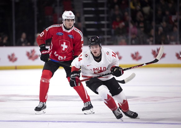 Switzerland&#039;s Lian Bichsel, left, and Canada&#039;s Zach Dean watch as the puck clears the Canadian zone during first-period IIHF World Junior Hockey Championship pretournament hockey game action ...