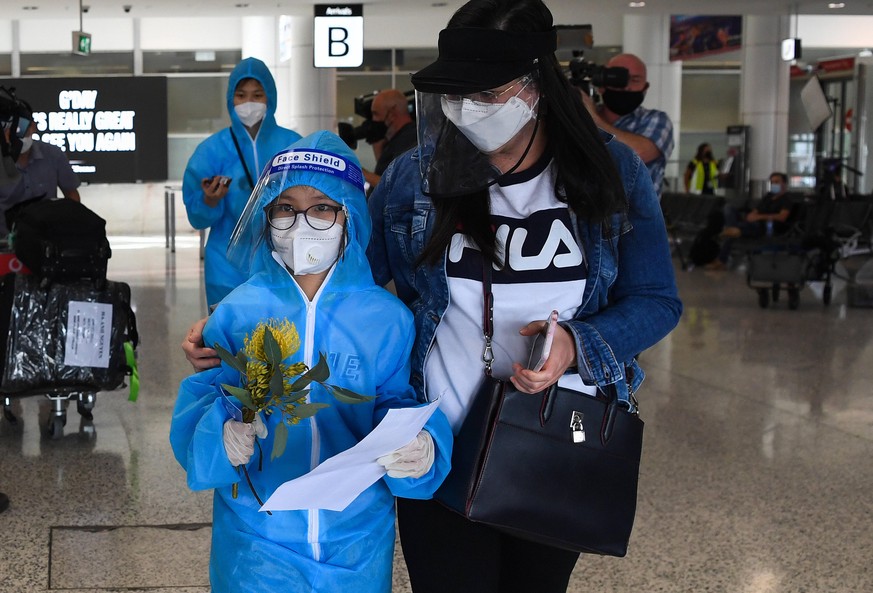 QUARANTINE FREE INTERNATIONAL ARRIVALS SYDNEY, A traveller dressed in full personal protection equipment (PPE) is greeted by family as they arrive on the first quarantine free international flights at ...