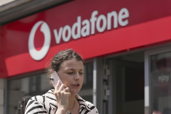 A woman talking on her mobile, walks past a Vodafone store in London, Wednesday, June 14, 2023. Vodafone and Three, which is owned by Hong Kong&#039;s CK Hutchison agreed Wednesday to merge their U.K. ...