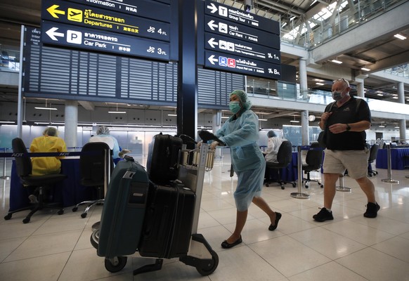 epa09544964 A hotel official wearing a protective suit escorts an international arriving passenger to a 14-day quarantine upon his arrival at the Suvarnabhumi Airport in Samut Prakan province, near Ba ...