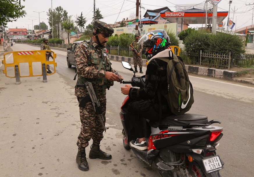 epa12087924 An Indian police and paramilitary soldier checks the identity card of a man at a temporary check point on a road leading to the airport after loud explosions were heard in Srinagar, the su ...