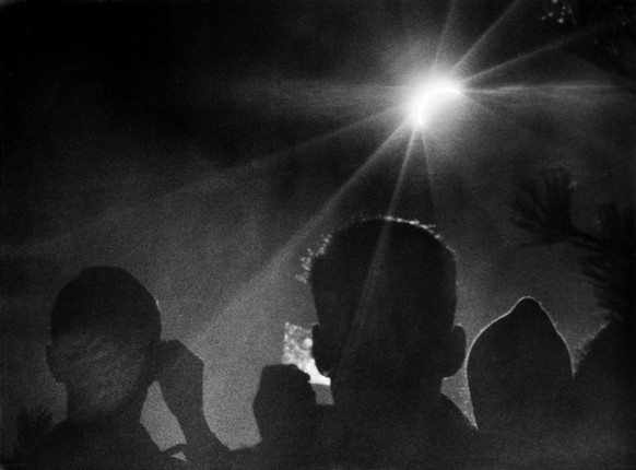 Personen betrachten mit rauchgeschwaerzten Glaesern die sich langsam total verfinsternde Sonne, aufgenommen am 15. Februar 1961 in der Naehe von Interlaken. (KEYSTONE/Hans-Ueli Bloechliger)