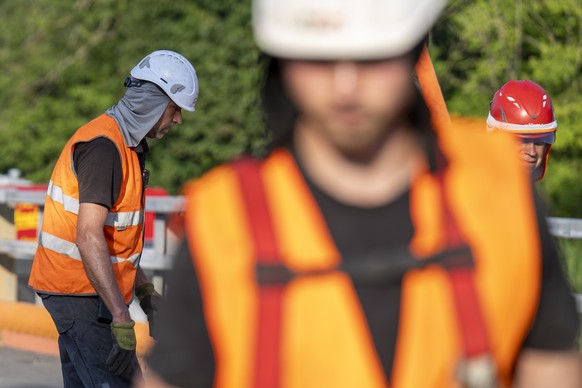 Bauarbeiter schuetzen sich mit Helm und Nackenschutz beim Einheben der Hilfsbruecke ueber die Sense, am Mittwoch, 31. Juli 2024, in Laupen. Bei der Verkehrssanierung und staedtebaulichen Entwicklung L ...