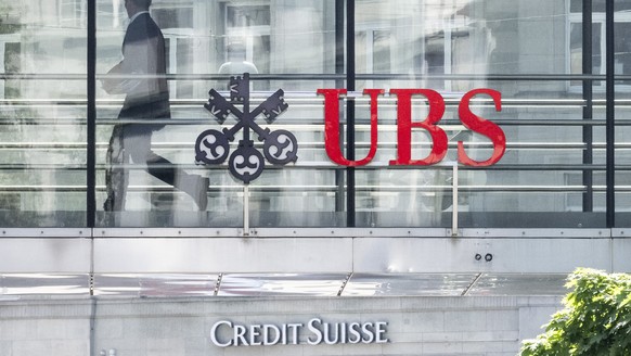 Ein Mann laeuft zwischen den beiden Logos der Banken UBS und Credit Suisse, aufgenommen am Montag, 12. Juni 2023 in Zuerich. Heute verkuendete die nunmehr einzige Schweizer Grossbank in einem offenen  ...