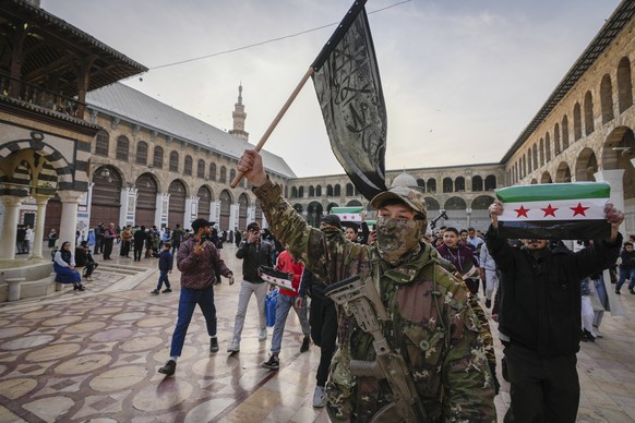 A masked opposition fighter carries a flag of Hayat Tahrir al-Sham (HTS) in the courtyard of the Umayyad Mosque in the old walled city of Damascus, Syria, on Tuesday, Dec. 10, 2024. HTS is the largest ...