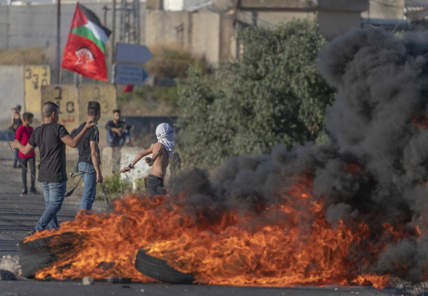 Palestinian protesters burn tires and use slingshots during clashes with Israeli soldiers at the entrance the Jewish settlement of Beit El, background, near the West Bank city of Ramallah, Tuesday, Ju ...