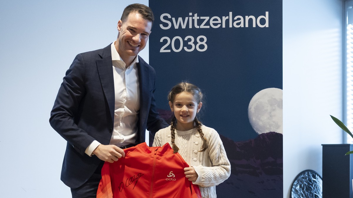 Dario Cologna, Vorstandsmitglied Switzerland 2038 und Vertreter der Athleten, uebergibt der jungen Langlauf-Athletin Malena Mueller eine Jacke, die er bei Olympia getragen hat, waehrend einer Medienko ...