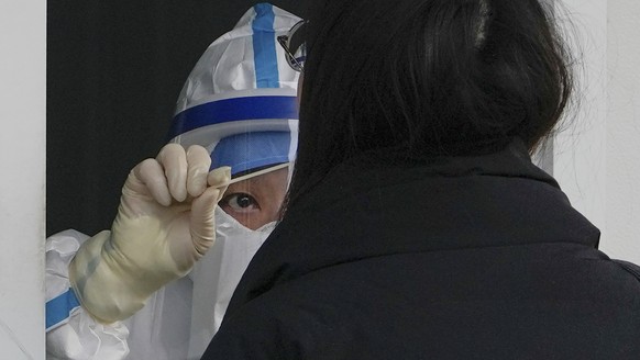 A worker in protective gear collects a sample from a resident at a coronavirus testing site inside a hospital compound in Beijing, Thursday, Dec. 15, 2022. China said Wednesday that it would stop repo ...