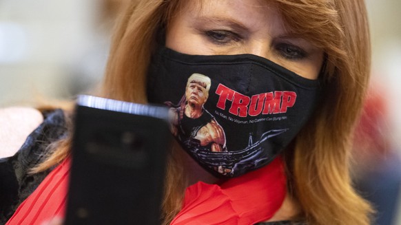 epa08797426 A woman takes a selfie of her self wearing a Rambo style Trump mask while attending an election night rally for Republican Senator from Georgia Kelly Loeffler, held in Atlanta, Georgia, US ...