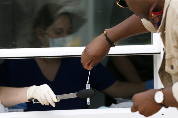 Parkland Hospital employees, sitting behind window, collect a self administered test sample from a man at a COVID-19 walk up testing site in Dallas, Thursday, June 11, 2020. The walk ups have extended ...