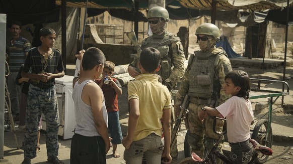 FILE - In this Sept. 15, 2017 file photo, Russian soldiers escorting a group of journalists stand guard as children gather, in Deir ez-Zor, Syria. After watching for years as the United States called  ...