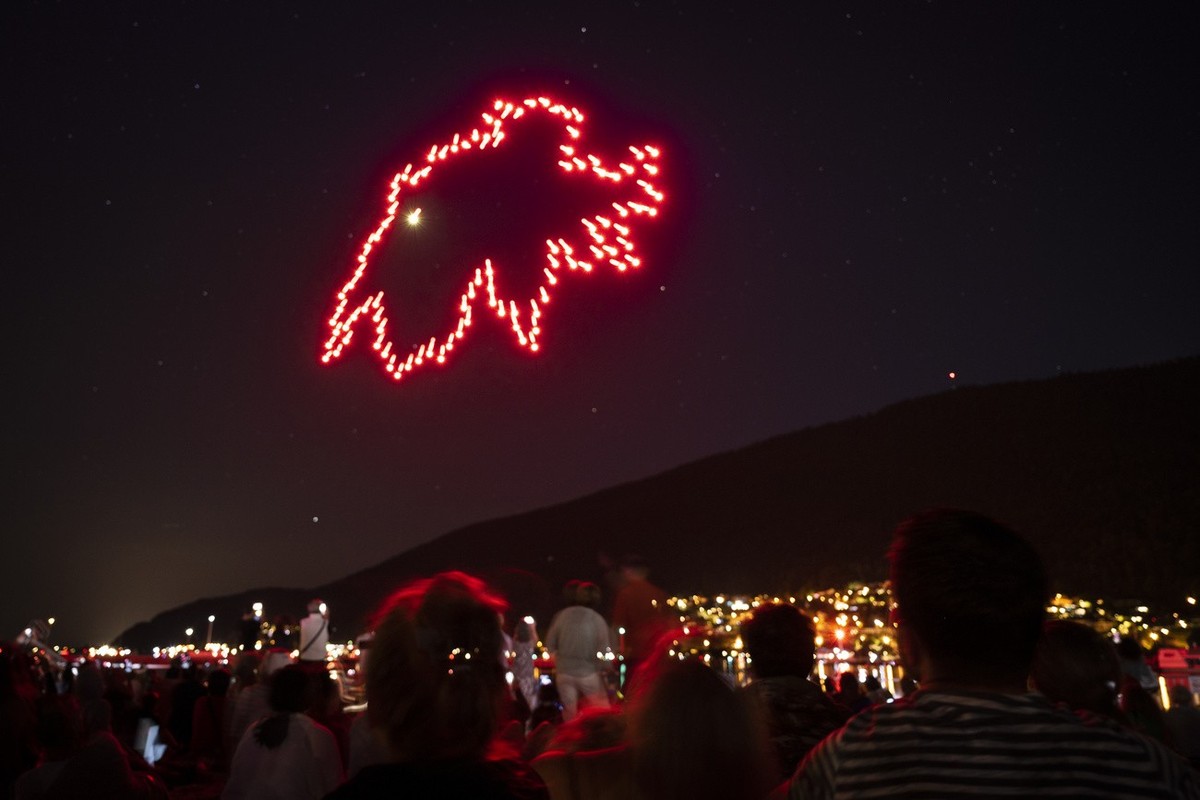Des personnes regardent un spectacle de drones depuis les bords du lac de Bienne, ce dimanche 31 juillet 2022 a Bienne. Cette choregraphie aerienne remplace les traditionnelles feux d'artifice du ...